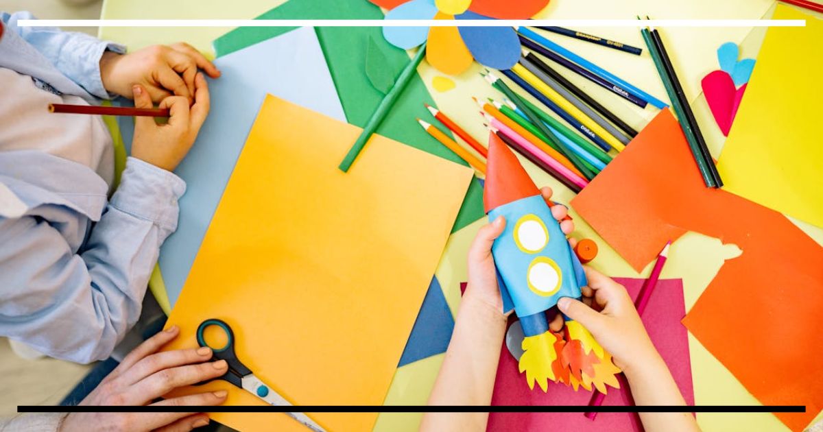 Crianças montando um foguete de papel colorido em uma mesa repleta de lápis, tesoura e folhas, representando a criatividade e o aprendizado por meio do brincar.