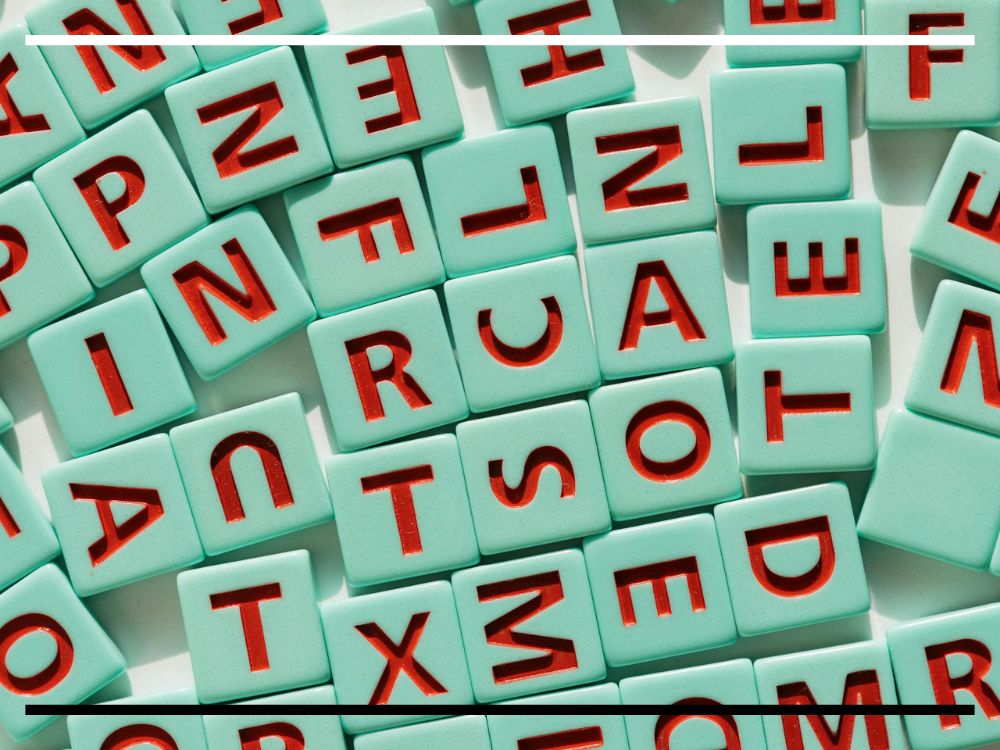 Um conjunto de peças quadradas verde-menta com letras vermelhas em relevo, dispostas de forma desorganizada. Algumas letras estão de cabeça para baixo ou inclinadas.