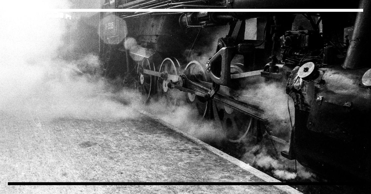 Rodas e bielas de locomotiva a vapor em movimento com fumaça.