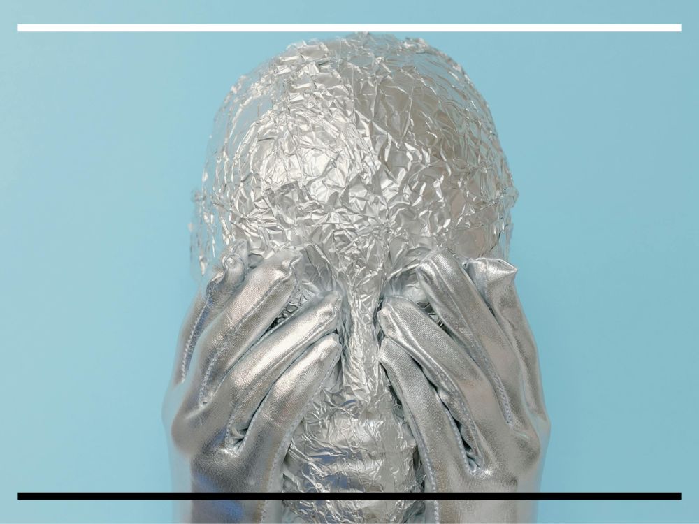 Cabeça humana coberta com papel alumínio e mãos metálicas apoiadas no rosto.
