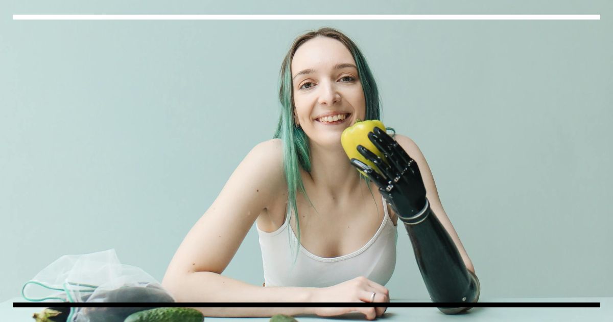 Mulher sorrindo com prótese no braço segura um pimentão amarelo sobre uma mesa.