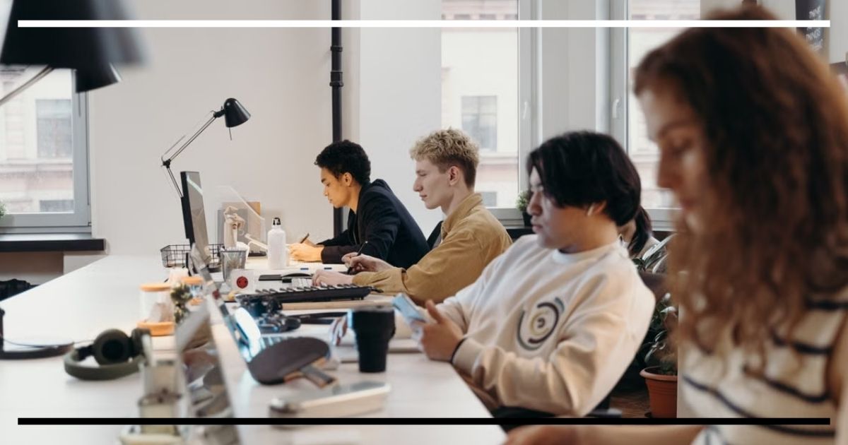Pessoas trabalhando sentadas diante de computadores e celulares em um escritório compartilhado.