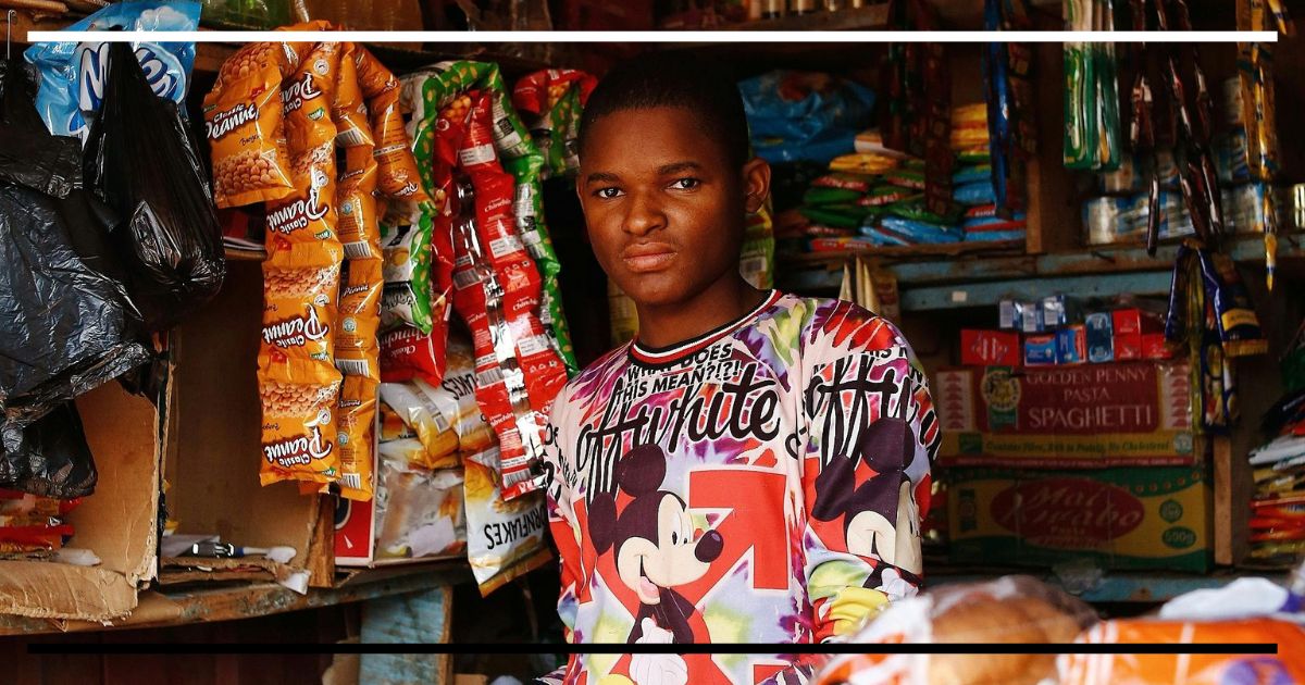 Jovem em mercearia cercado por produtos, representando o cotidiano material das relações sociais.