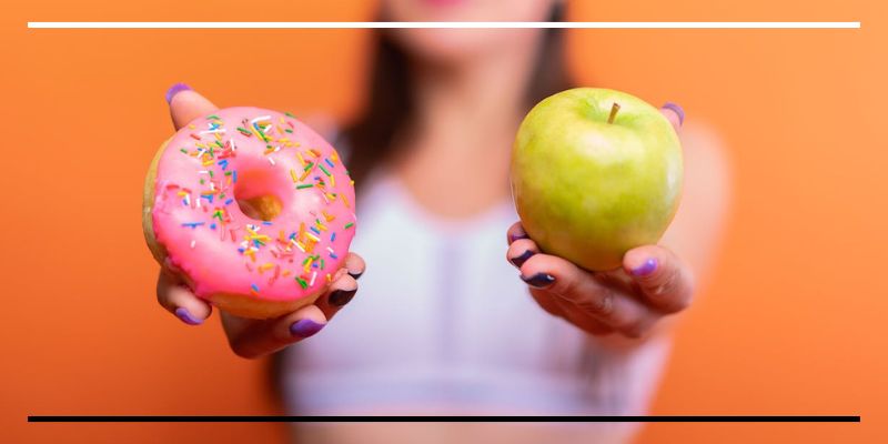 Pessoa segurando um donut colorido em uma mão e uma maçã verde na outra, simbolizando uma escolha.