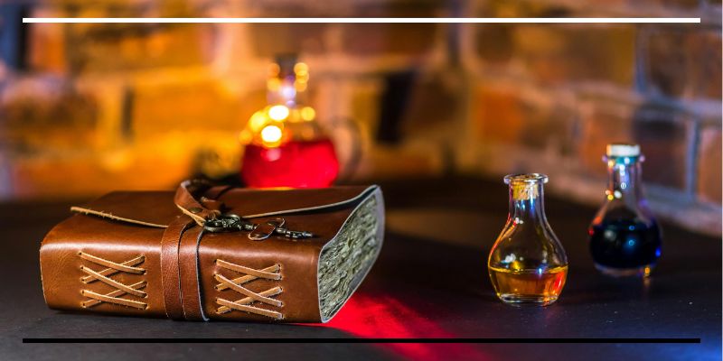 Caderno antigo de couro e frascos de líquidos coloridos sobre mesa.