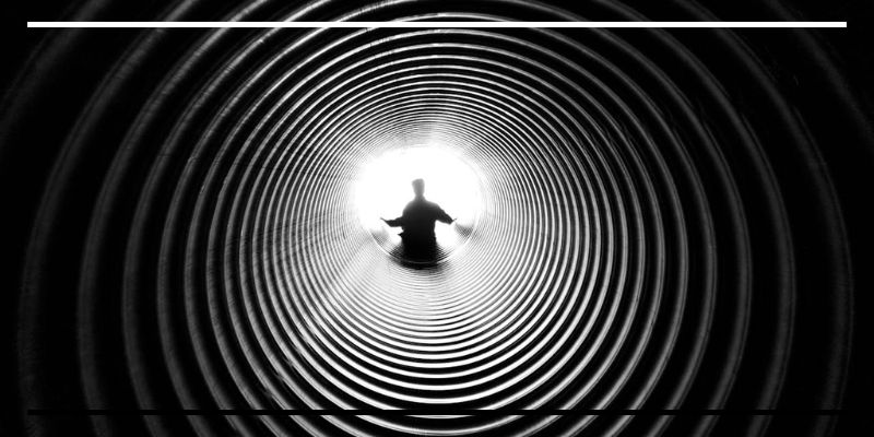Silhueta humana em túnel circular iluminado ao fundo.