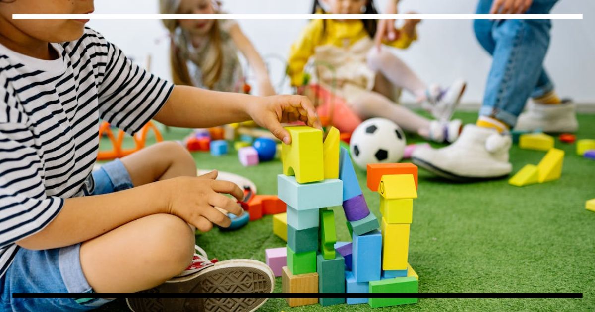 Crianças brincando em grupo com blocos coloridos no chão de uma sala de Educação Infantil, desenvolvendo cooperação e criatividade.