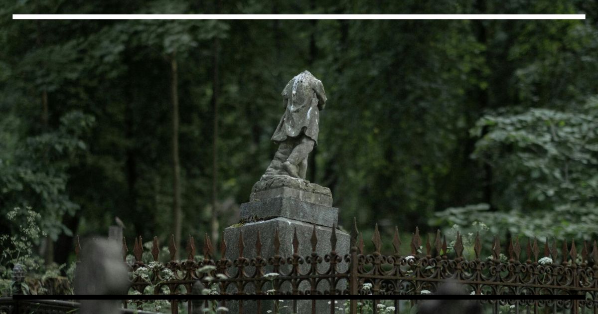 Estátua sem cabeça cercada por grades enferrujadas em um bosque, simbolizando o corpo fragmentado e sem controle da criatura de Frankenstein.