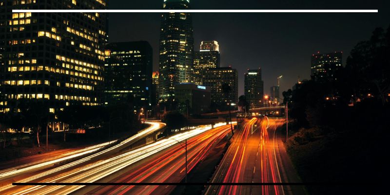 Tráfego urbano noturno com rastros de luz, simbolizando a aceleração e simultaneidade da sociedade em rede.