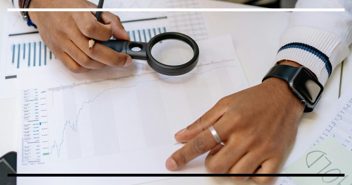 Mão com lupa analisando gráfico de desempenho financeiro.