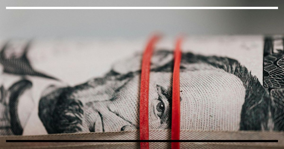 Close-up de cédula de dólar presa por elásticos, simbolizando moeda ancorada e intervenção cambial.