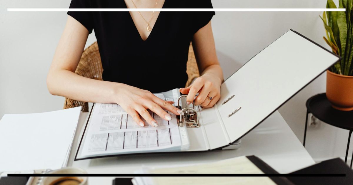 Analista folheando pasta de relatórios e séries históricas, representando modelos de câmbio de longo prazo e fundamentos.