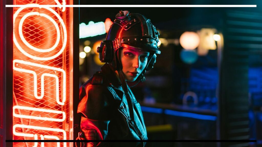Pessoa com capacete preto com rebites e fones laterais, jaqueta de couro, ao lado de letreiro de néon vermelho; fundo noturno com luzes desfocadas; olhar direto para a câmera.