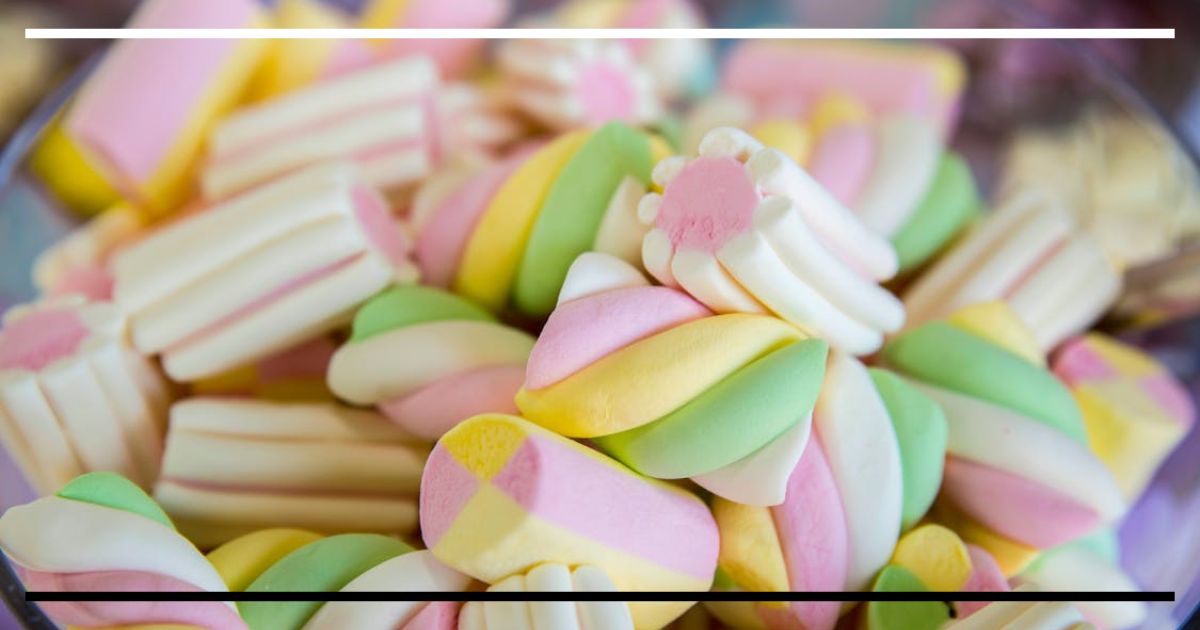 Close-up de marshmallows coloridos em tigela de vidro, tons pastel.