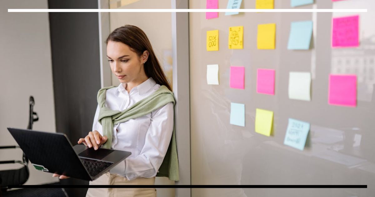 Pessoa usando notebook ao lado de parede com post-its coloridos em escritório.