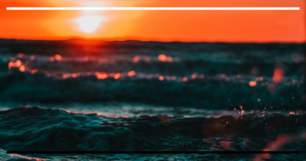 Mar ao entardecer em tons de laranja e ciano, com ondas em primeiro plano e profundidade de campo rasa.