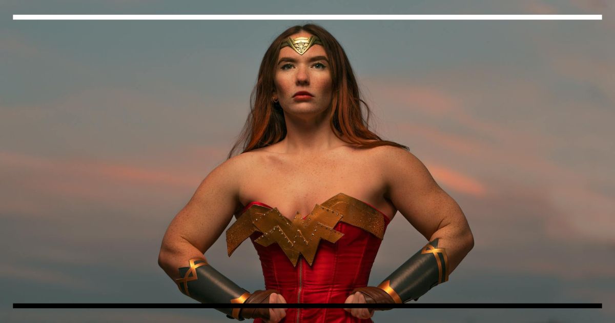 Mulher em cosplay de Mulher-Maravilha, mãos na cintura em postura expansiva, olhando à frente ao entardecer.