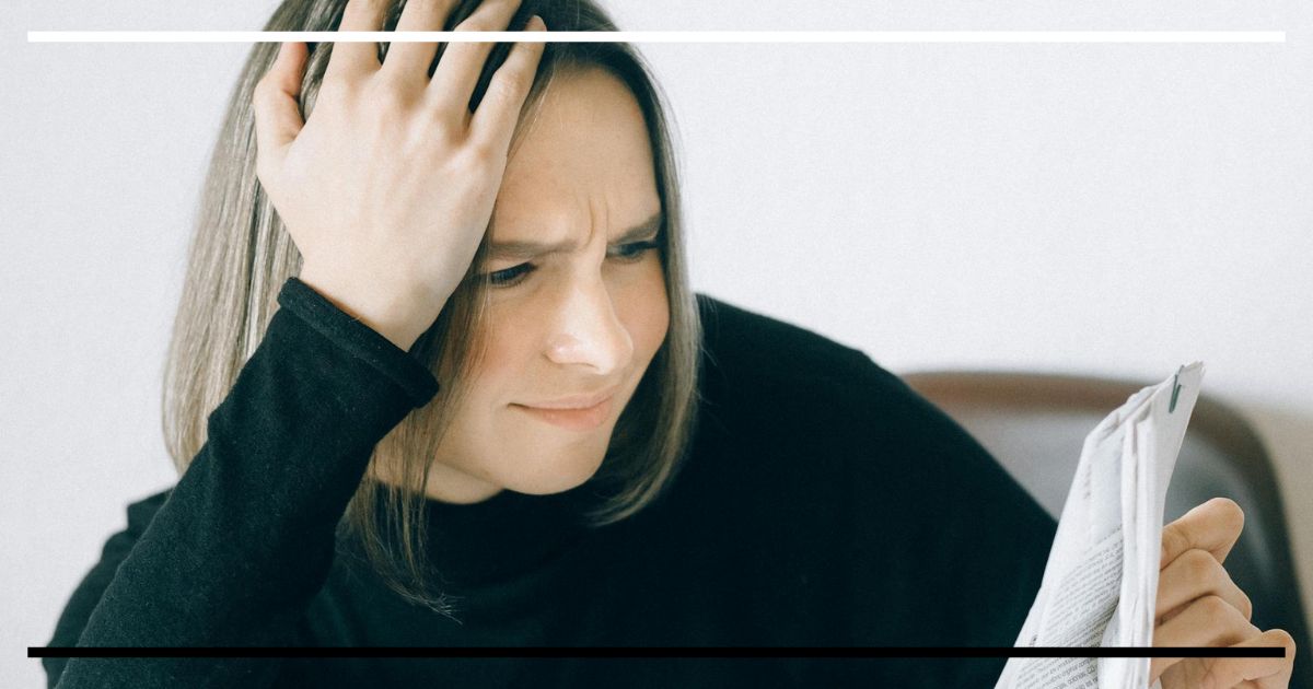 Pessoa franze a testa ao ler um artigo científico impresso, mão na cabeça.