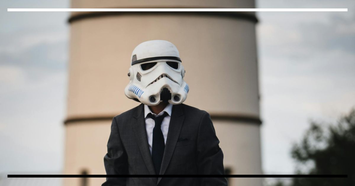Pessoa de terno usando capacete de stormtrooper, em ambiente urbano, foco no contraste entre fantasia e cotidiano.