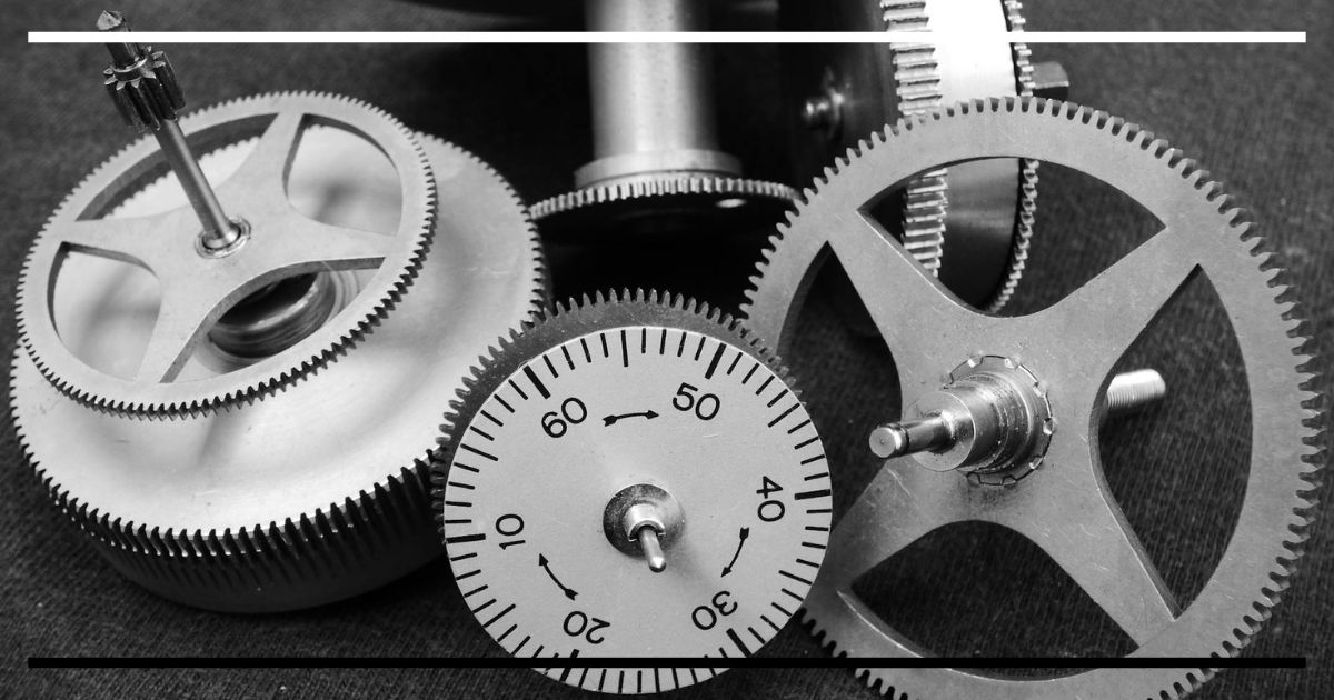 Conjunto de engrenagens metálicas e um mostrador circular de relógio, visto em close, em preto e branco, com numerais de 0 a 60.