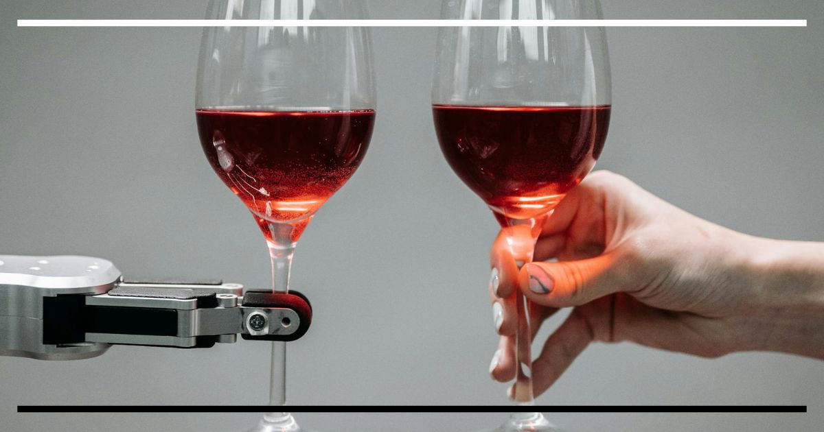Garra robótica e mão humana erguendo taças de vinho em brinde.
