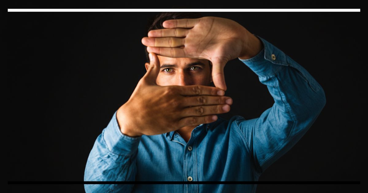 Homem em camisa azul enquadrando algo com as mãos.