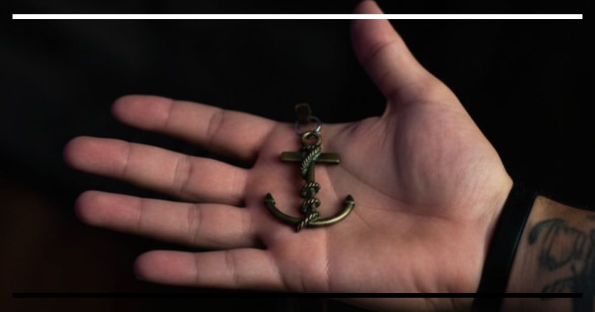 Mão segurando um pequeno pingente em forma de âncora.
