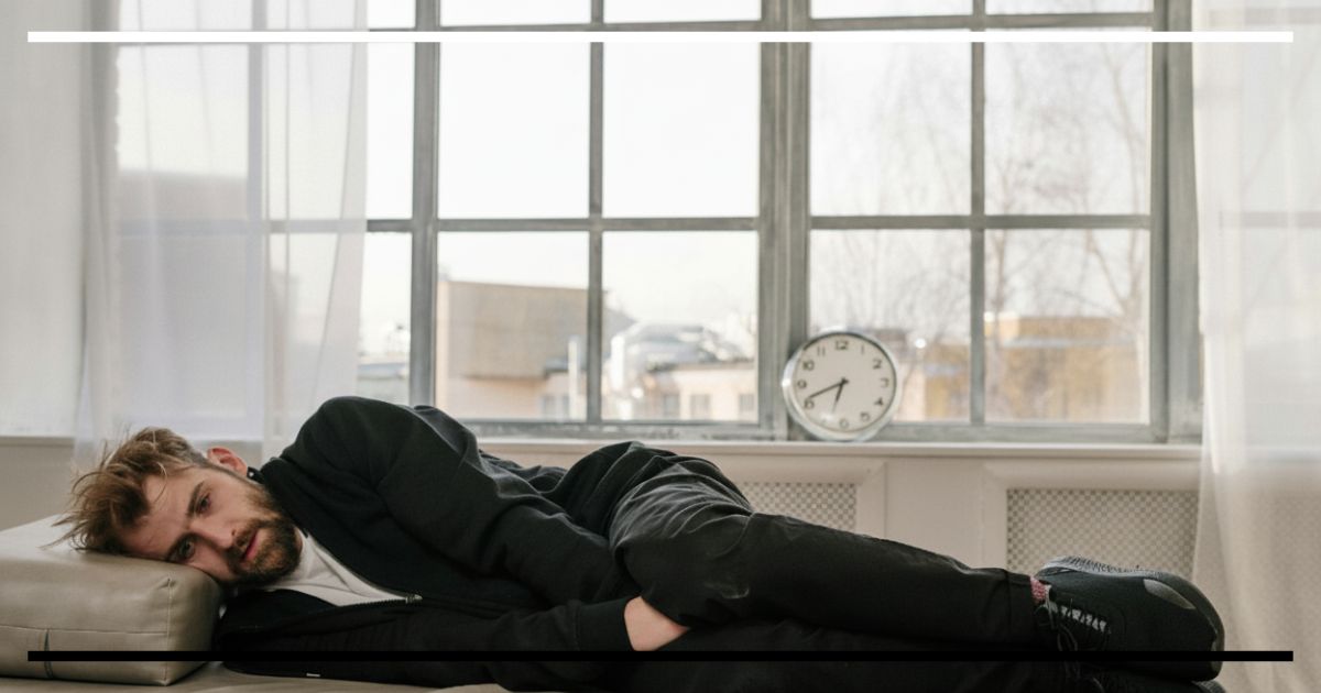 Pessoa deitada em ambiente iluminado com relógio ao fundo, simbolizando o envelhecimento celular e o cansaço sistêmico.