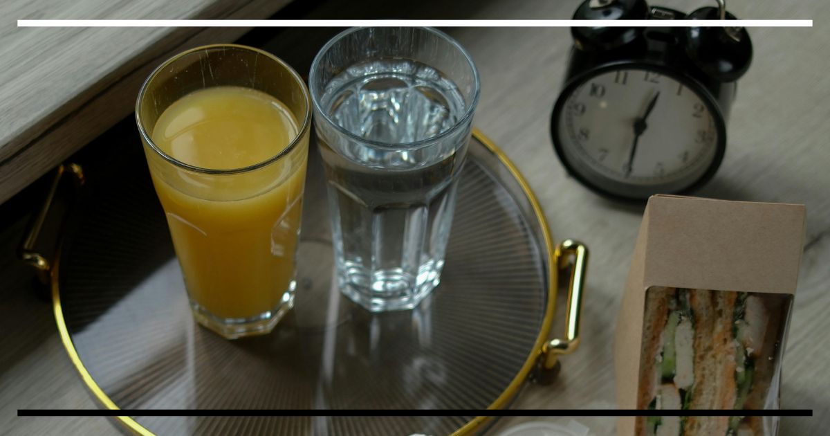 Copos de suco e água sobre bandeja com relógio ao fundo, simbolizando a prática do jejum intermitente.