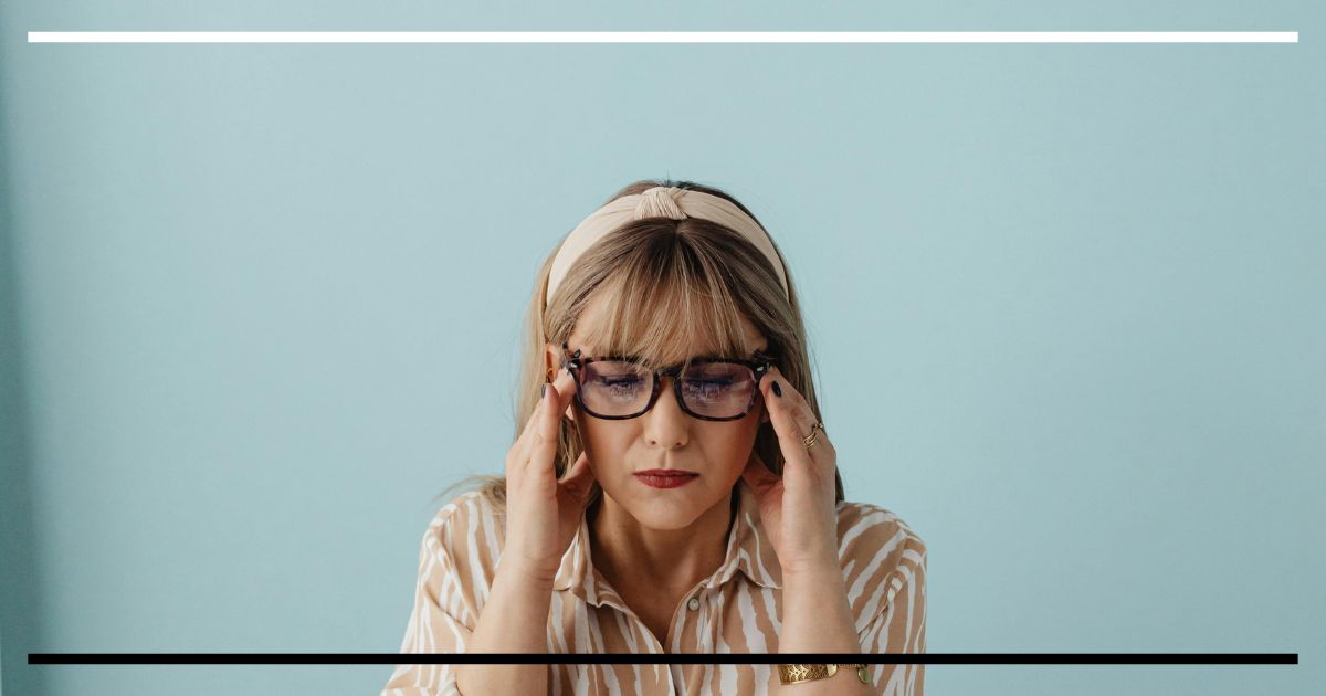 Mulher tocando as têmporas, concentrada, em fundo azul claro.