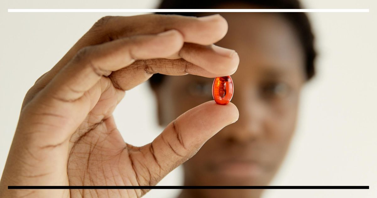 Pessoa segurando uma cápsula vermelha entre os dedos, foco no suplemento.