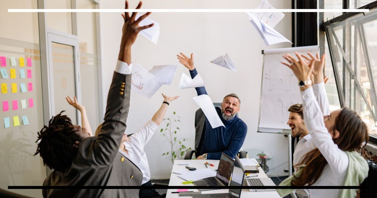 Equipe de escritório comemorando, jogando papéis para o alto, simbolizando sucesso coletivo.
