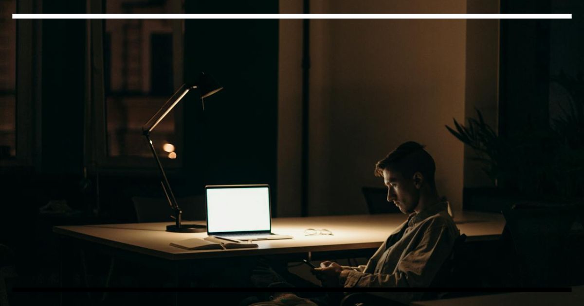 Burocracia e o custo de ser um outlier - homem isolado diante do laptop em ambiente escuro.