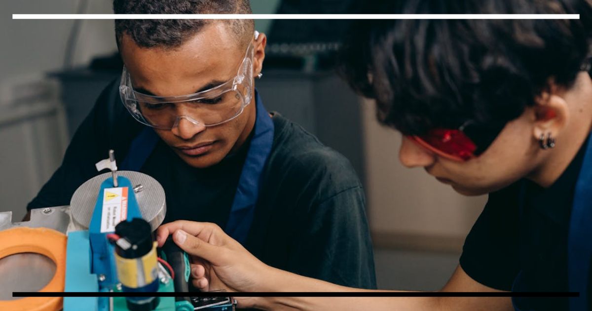 Dois estudantes manipulando equipamento técnico em atividade prática com uso de óculos de proteção.