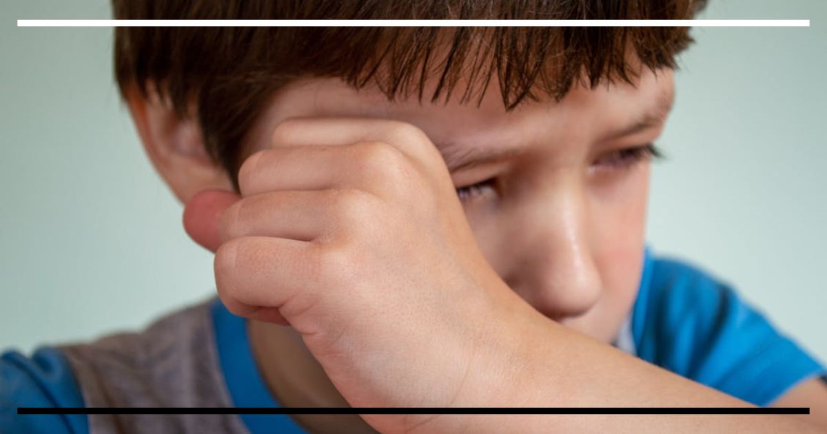 Criança pequena com expressão de frustração ou tristeza, com a mão no rosto, representando o momento de desregulação emocional durante uma birra.
