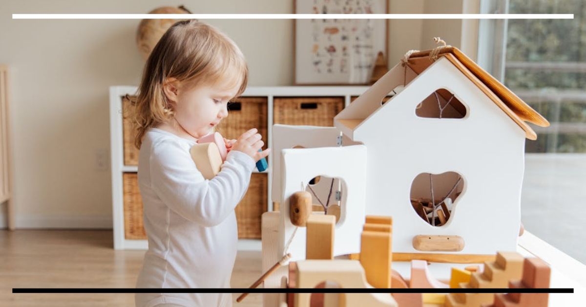 Criança pequena brinca concentrada com uma casa de bonecas de madeira e blocos, desenvolvendo funções executivas em um ambiente de aprendizado.