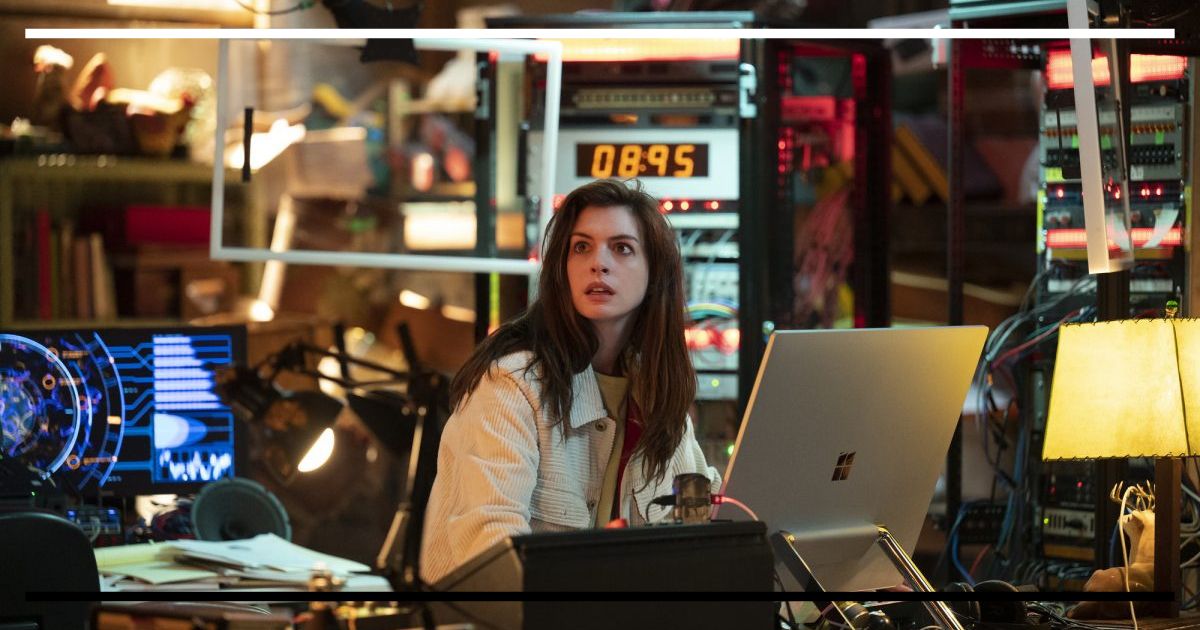 Cena do episódio Solos com Anne Hathaway (Leah). Ela está sentada em um laboratório caseiro desorganizado, cercada por equipamentos eletrônicos e cabos, com expressão de ansiedade enquanto olha para uma tela brilhante.