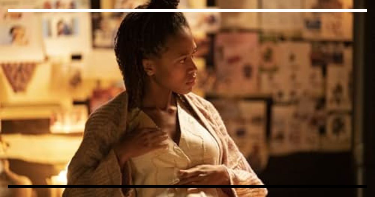 Nicole Beharie (Nera) grávida, em um ambiente rústico com pouca luz, segurando a barriga com as duas mãos e olhando para o lado com expressão de desconfiança e medo.