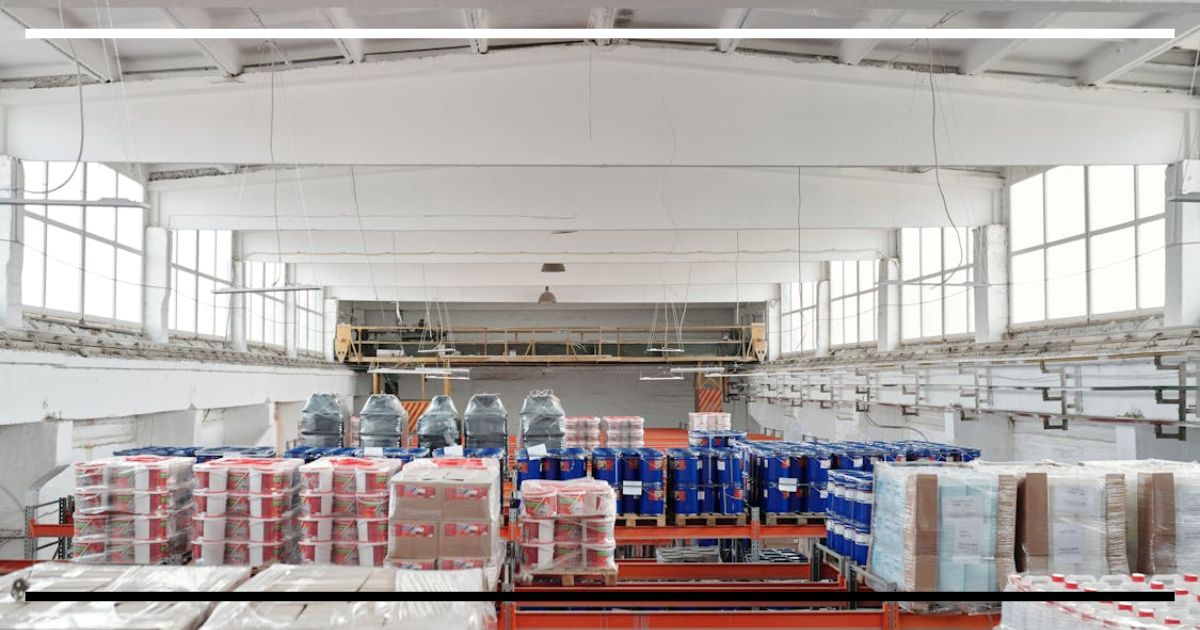 Interior de galpão industrial com produtos embalados em pallets e tambores empilhados, sugerindo produção e estoque no contexto da política comercial.