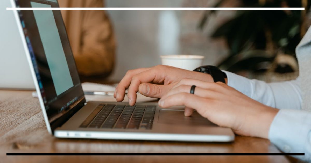 Pessoa digitando em notebook sobre mesa de madeira em ambiente de trabalho ou estudo