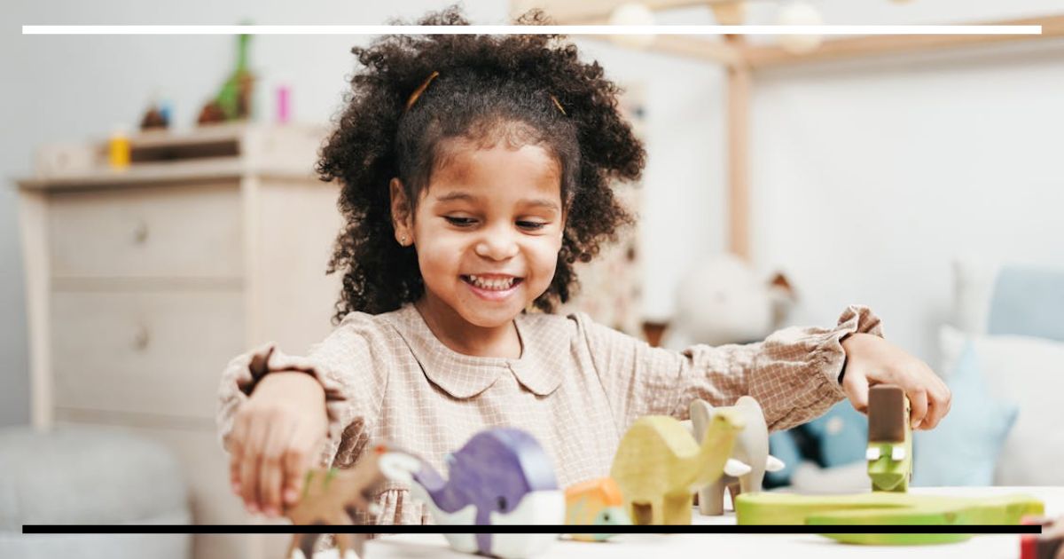 Criança sorrindo enquanto organiza figuras de animais de madeira sozinha, demonstrando concentração e autonomia no brincar solitário.