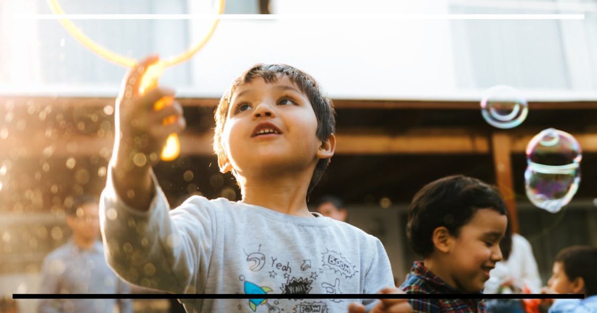 Criança com braço erguido alcançando bolhas de sabão ao ar livre, em momento de brincar livre – expressão de alegria, espontaneidade e autonomia infantil