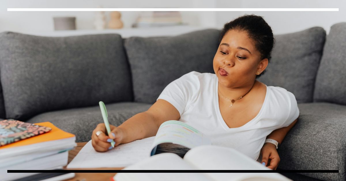 Estudante concentrada escrevendo em caderno com livros abertos, ilustrando o conceito de dificuldade desejável no aprendizado.