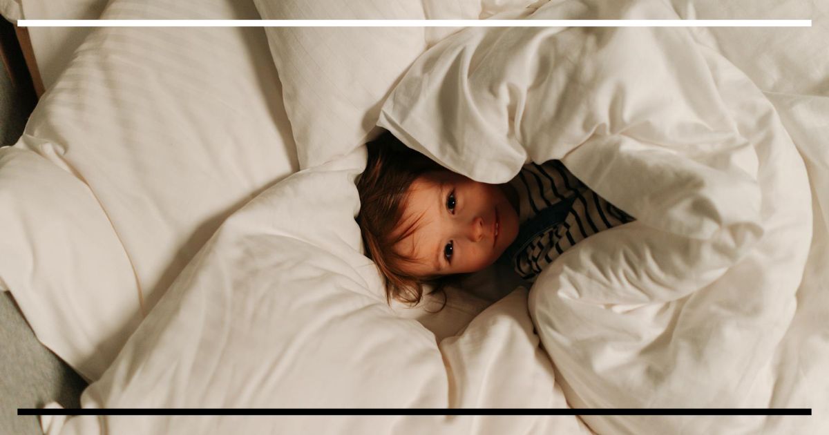 Criança pequena espiando entre lençóis brancos ao acordar, ilustrando a importância do sono infantil para o desenvolvimento das funções executivas.