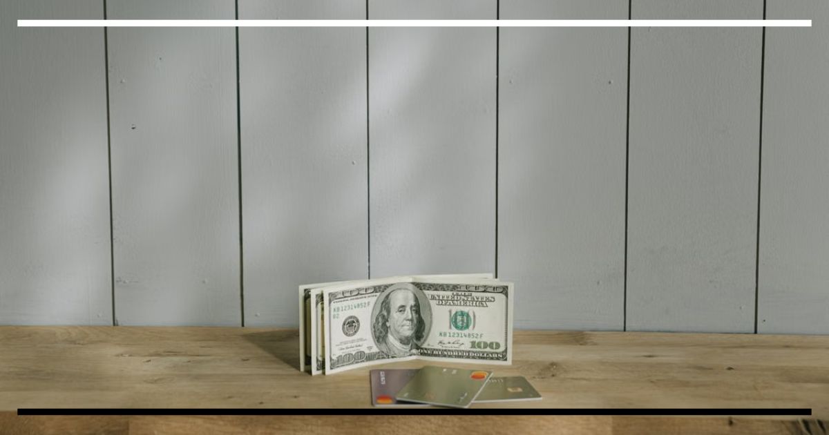 Cédulas de dólar e cartões bancários sobre uma mesa, representando o repasse da alta do câmbio para os preços internos.